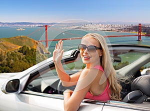 Happy young woman in convertible car waving hand