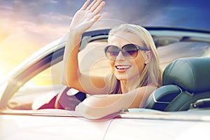 Happy young woman in convertible car waving hand