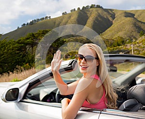 Happy young woman in convertible car waving hand