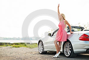 Happy young woman in convertible car waving hand