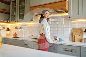 Happy young woman cooking coffee in cezve cup on kitchen