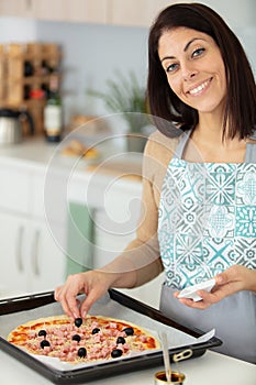 happy young woman cooking pizza at home in oven