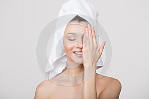 Happy young woman covers part of her face with her hand. A towel on her head. White background