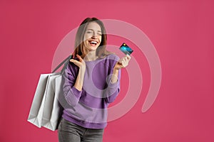 Happy young woman with credit card and bags on pink background, space for text. Spending money
