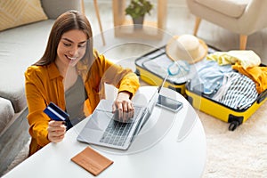 Happy young woman with credit card booking vacation at travel agency or making hotel reservation online, using laptop