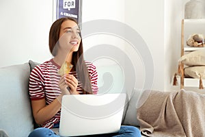 Happy young woman with credit card and laptop after online shopping at home