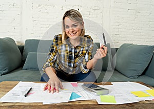 Happy young woman with credit card surrounded by papers calculating and paying bills