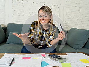 Happy young woman with credit card surrounded by papers calculating and paying bills