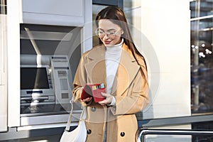 Happy young woman with credit cards near cash machine outdoors