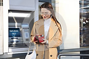 Happy young woman with credit cards near cash machine outdoors