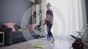 Happy young woman cute housewife is washing floor with mop and dancing at home