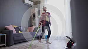 Happy young woman cute housewife is washing floor with mop and dancing at home