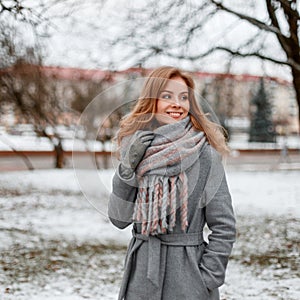 Happy young woman with a cute smile in warm gloves in a winter fashionable coat with a knitted vintage scarf posing