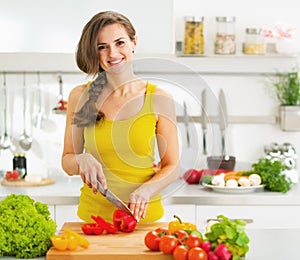 Happy young woman cutting fresh vegetable salad