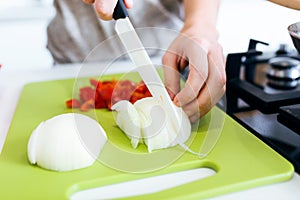 Happy young woman cutting fresh vegetables in kitchen