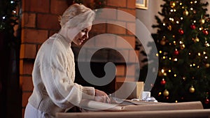 Happy young woman cutting wrapping craft paper with scissors to wrapping gift boxes of Christmas presents for family