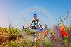 Happy young woman cyclist riding a mountain bicycle in summer field. Girl having fun lifting legs