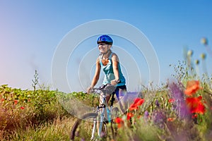 Happy young woman cyclist riding a mountain bicycle in summer field. Girl having fun lifting legs