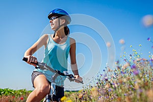 Happy young woman cyclist wearing helmet having rest after riding bicycle in summer field enjoying landscape