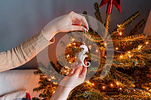 Happy young woman decorating christmas tree at home. Winter holidays in a house interior. Golden and white Christmas