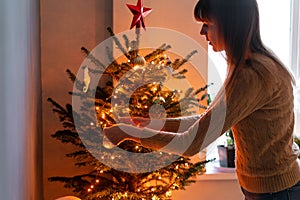 Happy young woman decorating christmas tree at home. Winter holidays in a house interior. Golden and white Christmas