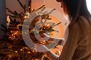 Happy young woman decorating christmas tree at home. Winter holidays in a house interior. Golden and white Christmas