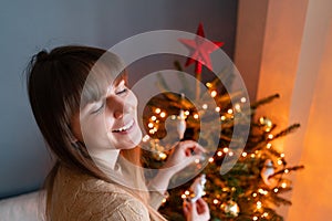 Happy young woman decorating christmas tree at home. Winter holidays in a house interior. Golden and white Christmas