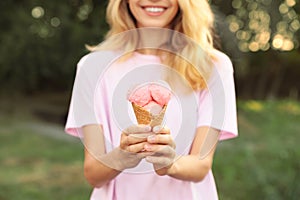 Happy young woman with delicious ice cream in waffle cone outdoors, closeup