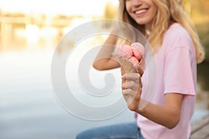 Happy young woman with delicious ice cream in waffle cone outdoors, closeup. Space for text