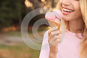 Happy young woman with delicious ice cream in waffle cone outdoors, closeup. Space for text