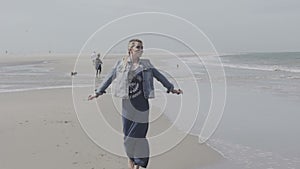 Happy young woman in denim jacket enjoying walk on lonely beach.