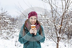 Happy young woman with disposable cup of coffee or tea wearing warm clothing. Beautiful girl holding disposable cup,standing