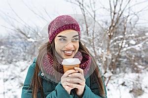 Happy young woman with disposable cup of coffee or tea wearing warm clothing. Beautiful girl holding disposable cup,standing