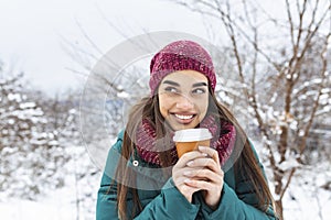 Happy young woman with disposable cup of coffee or tea wearing warm clothing. Beautiful girl holding disposable cup,standing