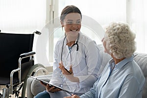 Happy young woman doctor consult disabled handicapped old grandma patient