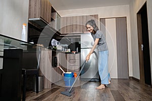 Happy young woman doing chores vacuuming the kitchen floor. Housekeeping concept