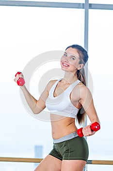 Happy young woman is doing exercises with dumbbells on step board.