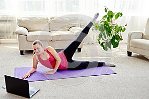 Beautiful young woman doing working out exercise on floor at home, online training on laptop computer, copy space.