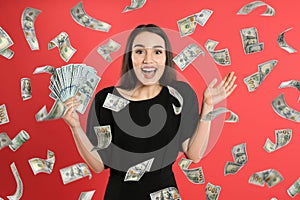 Happy young woman with dollars under money rain on background