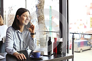 Happy young woman drinking cappuccino, latte, macchiato, tea, using tablet computer and talking on the phone in a coffee shop / ba