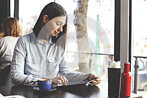Happy young woman drinking cappuccino, latte, macchiato, tea, using tablet computer and talking on the phone in a coffee shop / ba