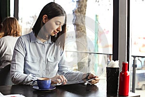 Happy young woman drinking cappuccino, latte, macchiato, tea, using tablet computer and talking on the phone in a coffee shop / ba