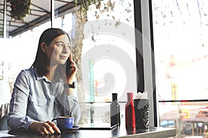 Happy young woman drinking cappuccino, latte, macchiato, tea, using tablet computer and talking on the phone in a coffee shop / ba