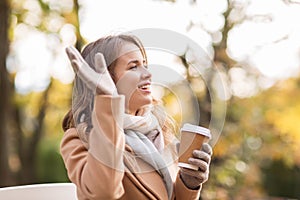 Happy young woman drinking coffee in autumn park