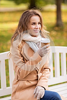 Happy young woman drinking coffee in autumn park