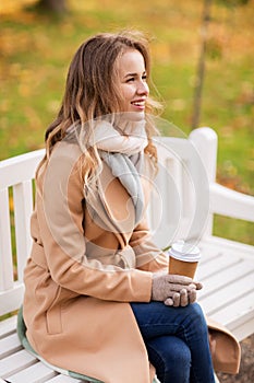Happy young woman drinking coffee in autumn park