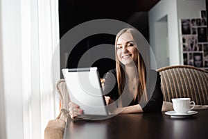 Happy young woman drinking coffee or tea and using tablet computer in a coffee shop