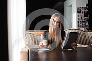 Happy young woman drinking coffee tea and using tablet computer in a coffee shop.