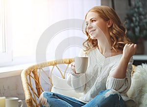 Happy young woman drinking morning coffee by window in winter