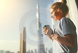 Happy young woman drinks coffee in morning at window